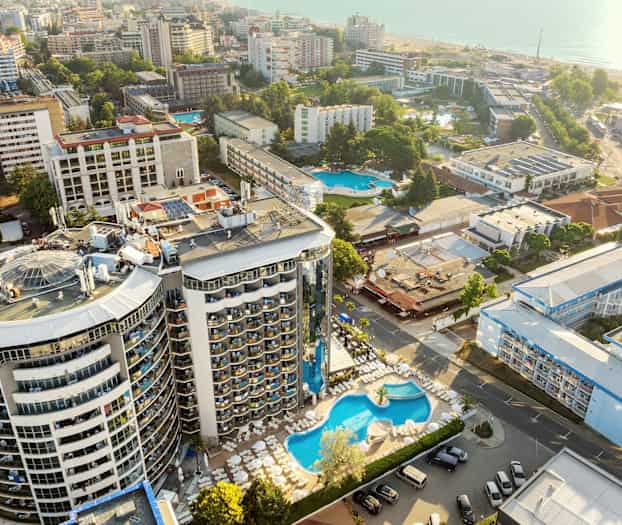 Flygfoto över hotellområde med pool och omgivande byggnader nära havet. (AI-genererad text)