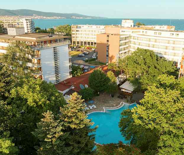 Hotellbyggnader med en pool omgivet av grönska, nära havet. (AI-genererad text)