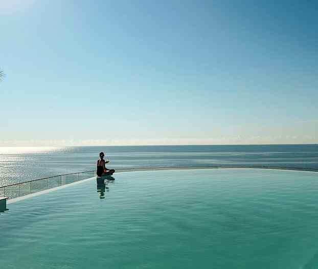 En person sitter vid kanten av en pool med havet i bakgrunden. (AI-genererad text)