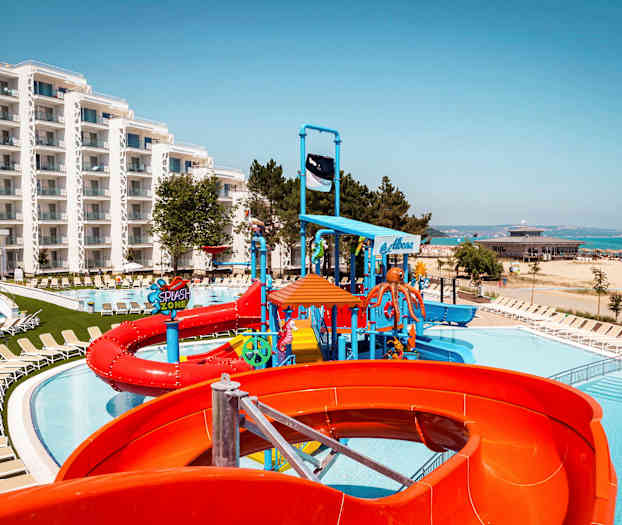 Bild av ett hotellområde med pool, vattenrutschbanor och liggstolar nära stranden. (AI-genererad text)