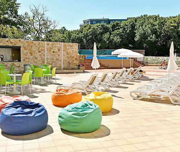 Solstolar och parasoller vid en pool, med färgglada sittpuffar och gröna stolar. (AI-genererad text)