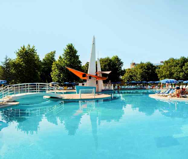 Öppen pool med bro och dekorativ båt mitt i, omgiven av solstolar och parasoller. (AI-genererad text)