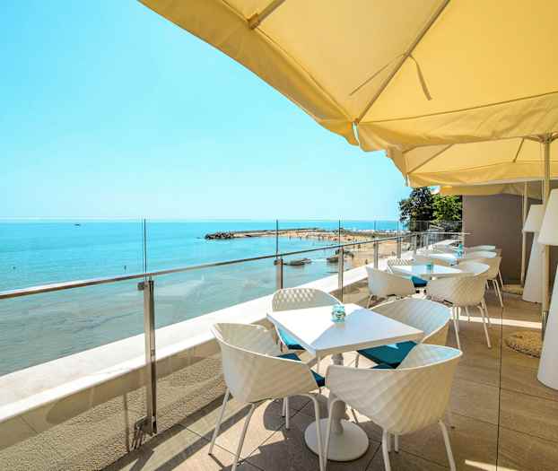 Terrass med bord och stolar under parasoll som vetter mot stranden och havet. (AI-genererad text)