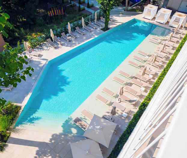 En bild av en pool med solstolar och parasoller runt omkring i en utomhusmiljö. (AI-genererad text)