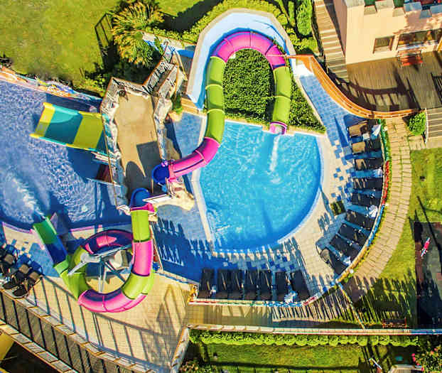 Luftbild av en pool med rutschkanor och solstolar runtom. (AI-genererad text)