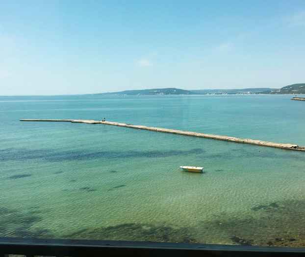 En brygga sträcker sig ut i det klara blå vattnet. En ensam båt ligger förtöjd vid ytan. (AI-genererad text)