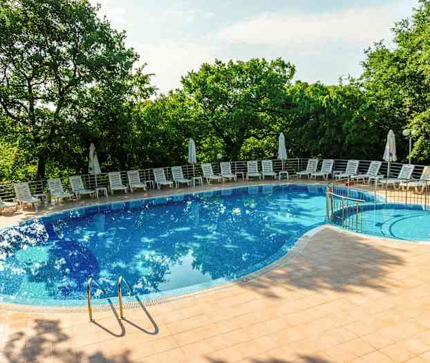 Bild av en utomhuspool omgiven av solstolar och parasoller, med gröna träd i bakgrunden. (AI-genererad text)