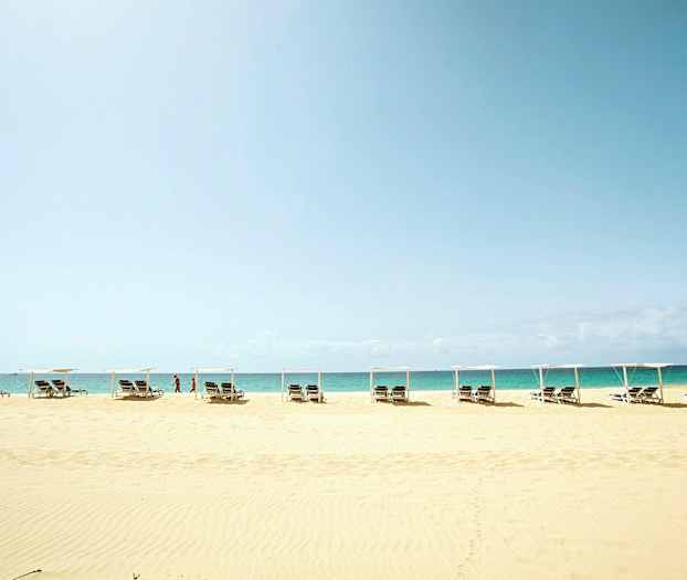 Strand med solstolar och parasoll framför havet. (AI-genererad text)