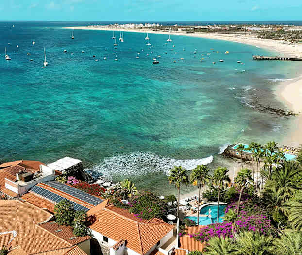 Utsikt över kust med palmer, turkost vatten och segelbåtar. (AI-genererad text)