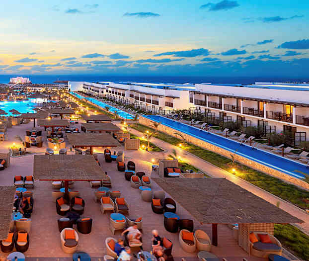 Ett hotellområde med pooler, eleganta sittplatser och byggnader vid solnedgång. (AI-genererad text)