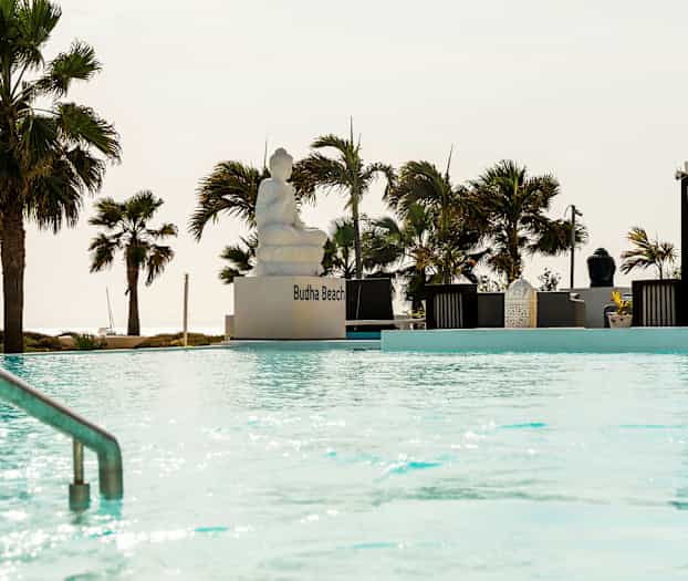 En utomhuspool med en sittande staty och omgivande spaljéer samt palmer. (AI-genererad text)