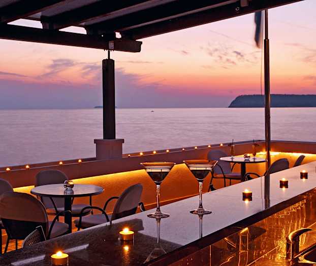 Uteservering med bord och stolar vid havet i solnedgången. (AI-genererad text)