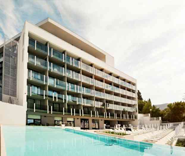 Ett modernt hotell med flera balkonger framför en pool. (AI-genererad text)