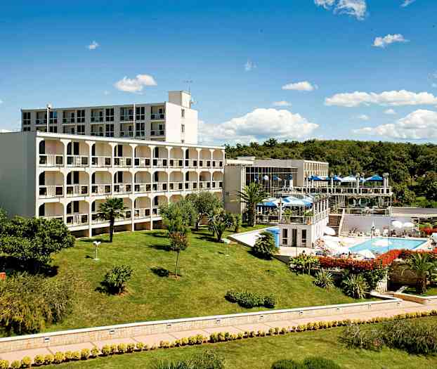 En byggnadskomplex omgiven av en välskött gräsmatta och trädgård, med en swimmingpool och uteserveringar. (AI-genererad text)