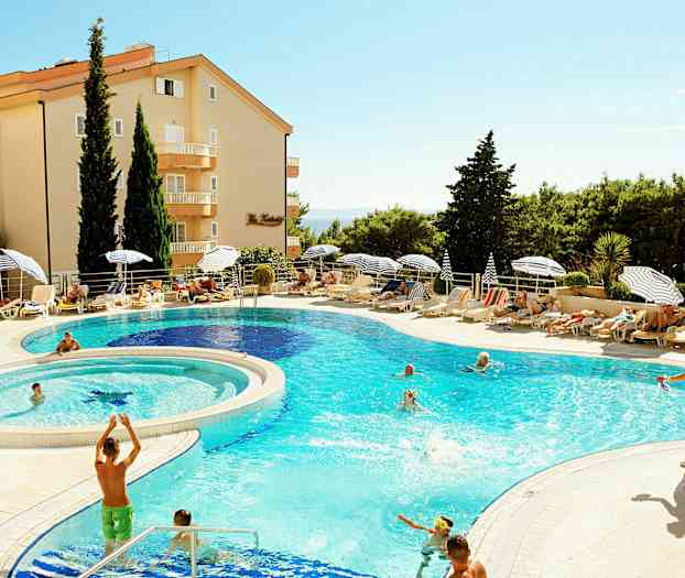 En semesteranläggning med en pool omgiven av solstolar, parasoll och gröna träd. (AI-genererad text)