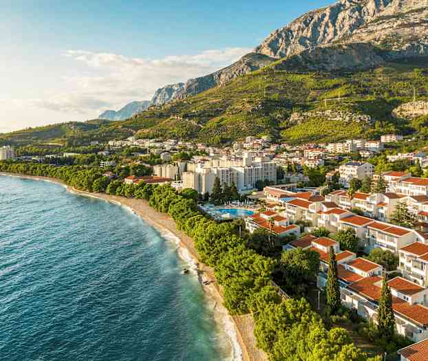 Flygfoto av kuststad framför grönskande berg. (AI-genererad text)