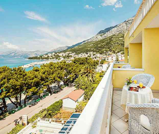 Utsikt från en gul byggnads balkong över en stad vid havet och omgivande berg. (AI-genererad text)