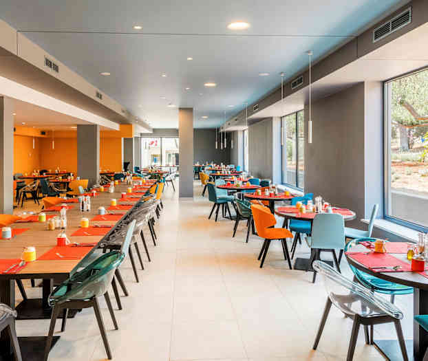 En modern matsal med stora fönster, färgglada stolar och dukade bord. (AI-genererad text)