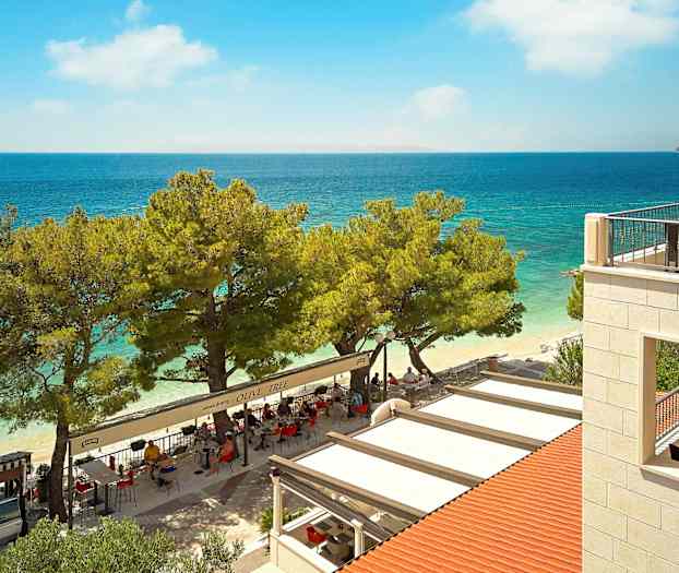 Utsikt över en restaurang vid stranden med havet i bakgrunden. (AI-genererad text)