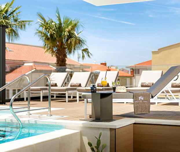 Poolområde med solstolar och bord nära en träplattform. (AI-genererad text)