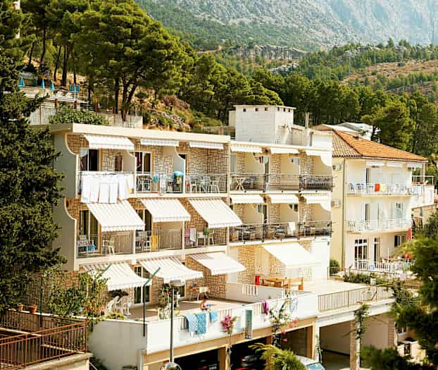 Vit byggnad med terrasser, belägen vid skogskant och bergen. (AI-genererad text)