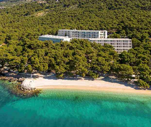 Hotellbyggnader omgivna av grönska nära en strand med klart turkost vatten. (AI-genererad text)