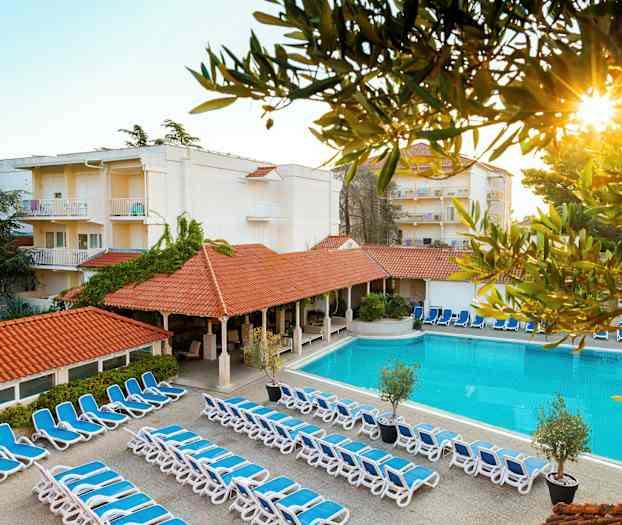 Bild av hotellområde med solstolar, pool och byggnader. (AI-genererad text)