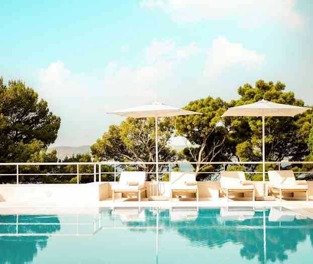 En utomhuspool omgiven av solstolar, parasoller och grönskande träd. (AI-genererad text)