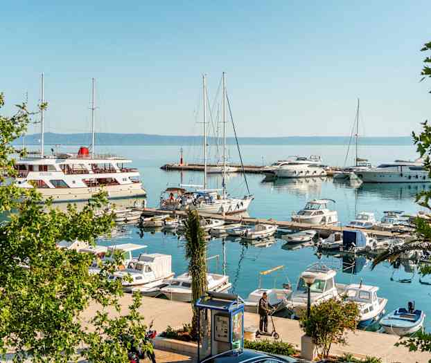En småbåtshamn med segelbåtar och motorbåtar. Enstaka människor står vid bryggorna. (AI-genererad text)