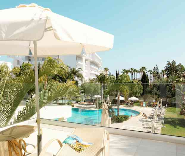 Vy från en terrass med parasoll, solstolar och utsikt över en pool och trädgård. (AI-genererad text)