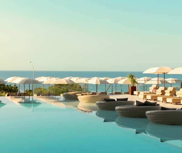 En infinitypool med liggstolar och parasoller vid havet. (AI-genererad text)