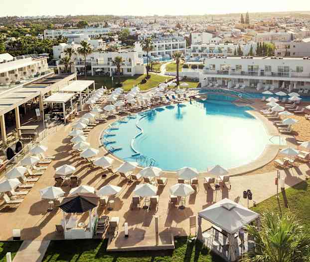 En stor utomhuspool omgivet av solstolar och parasoller, med hotellbyggnader i bakgrunden. (AI-genererad text)