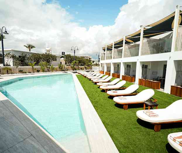 Utomhuspool med solstolar vid en hotellbyggnad. (AI-genererad text)