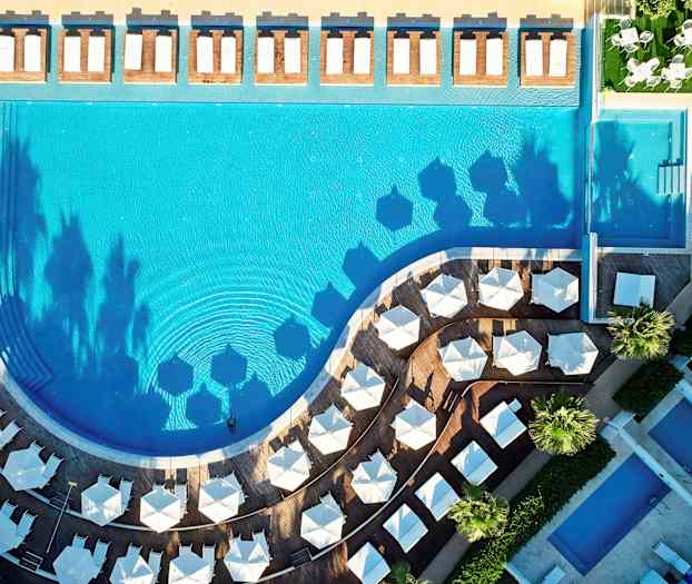 Fågelperspektiv av en pool med solstolar och parasoller kring den. (AI-genererad text)