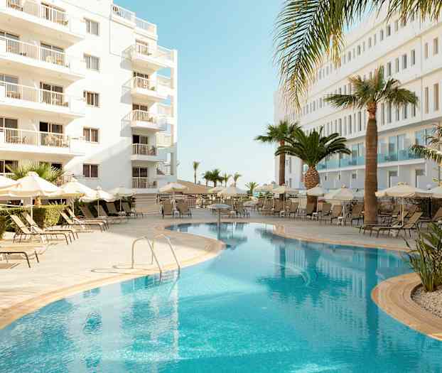 Utomhuspool med solstolar och paraplyer, omgiven av vita byggnader och palmer. (AI-genererad text)