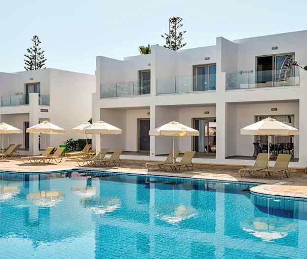 Vitmålade byggnader med terrasser vid poolområde med solstolar och parasoller. (AI-genererad text)
