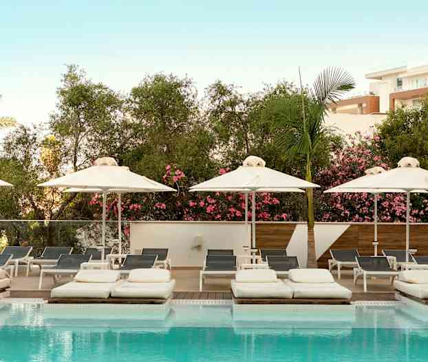 Bild på en pool med solsängar och parasoller, omgiven av vegetationsrikedom och en ljusblå himmel. (AI-genererad text)