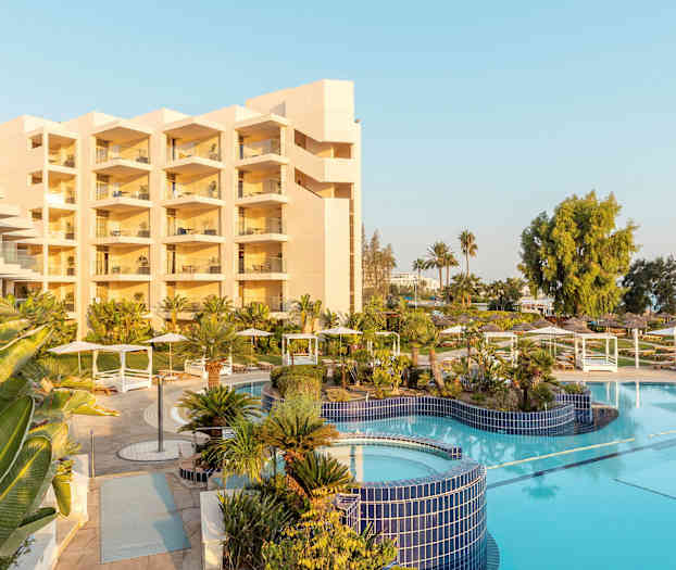 Hotellbyggnad med balkonger, poolområde och grönska. (AI-genererad text)