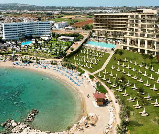 Vy över ett hotell med poolområde nära en sandstrand och turkost vatten. (AI-genererad text)