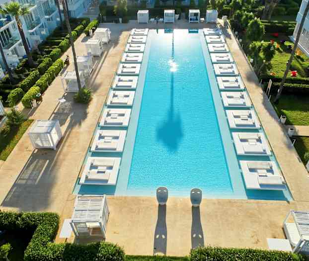 En rektangulär pool omgiven av solsängar och grönska. (AI-genererad text)