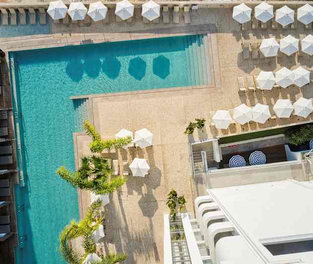 Flygbild över en pool med solstolar och parasoller omkring. (AI-genererad text)
