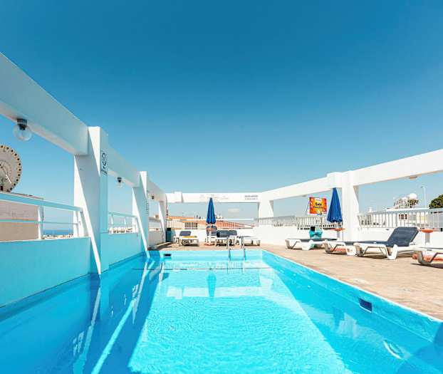 En utomhuspool med solstolar och parasoller under en klarblå himmel. (AI-genererad text)