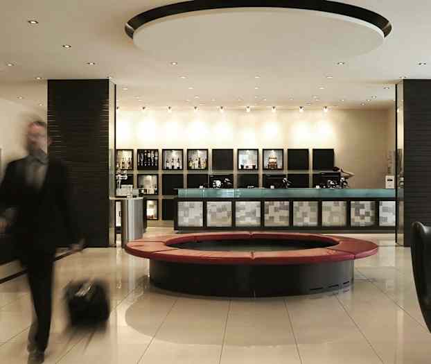 En välbelyst hotellobby med en reception, moderna sittplatser och ett runt soffområde. En person med bagage är i rörelse. (AI-genererad text)