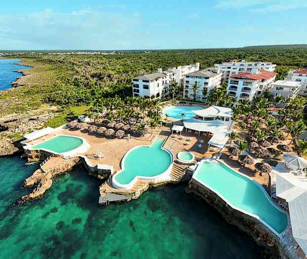 Flygbild över ett semesteranläggning med pooler och takparasoller vid havet. (AI-genererad text)