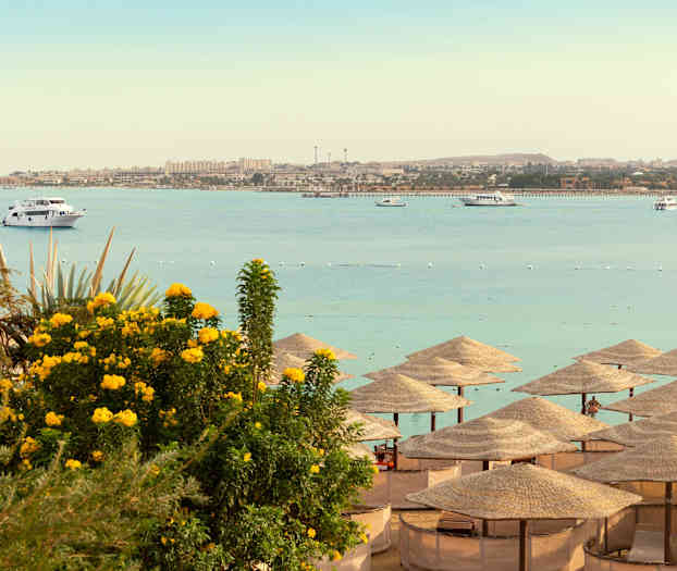 Strand med parasoller, havet och båtar i bakgrunden. (AI-genererad text)