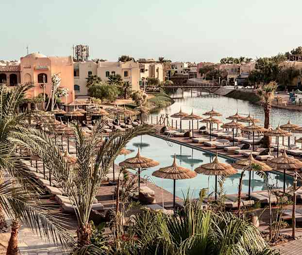 Poolområde med solstolar och parasoller, omgivna av palmer och byggnader. (AI-genererad text)