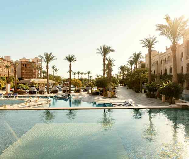 Hotellområde med utomhuspooler och rader av palmer vid sidan av byggnader. (AI-genererad text)