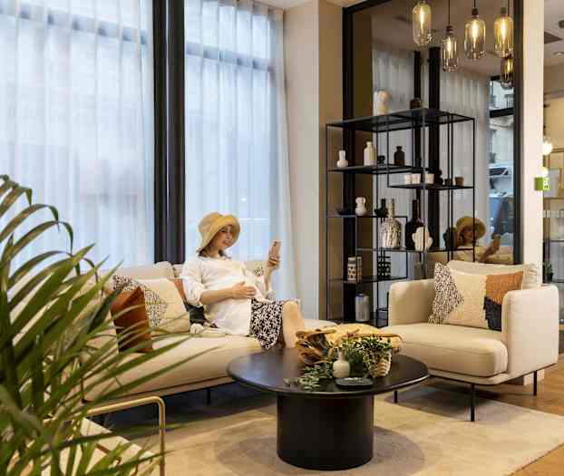 Sällskapsrum med soffa, bord och hylla med dekorationer, samt växt och glaslampor. (AI-genererad text)