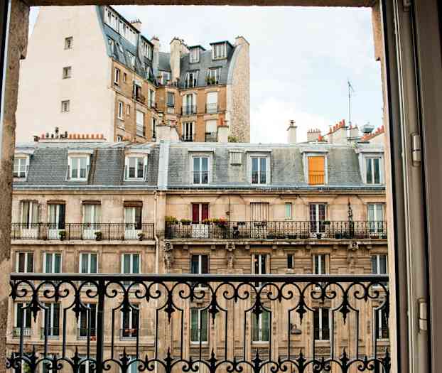 En bild av en byggnad med balkonger tagen från ett fönster med järnräcke. (AI-genererad text)