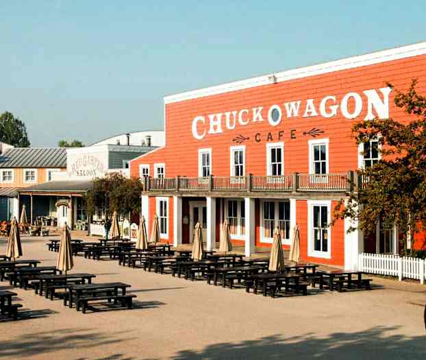 Ett område med bord och parasoller framför en byggnad med skylten 'Chuck Wagon Cafe'. (AI-genererad text)